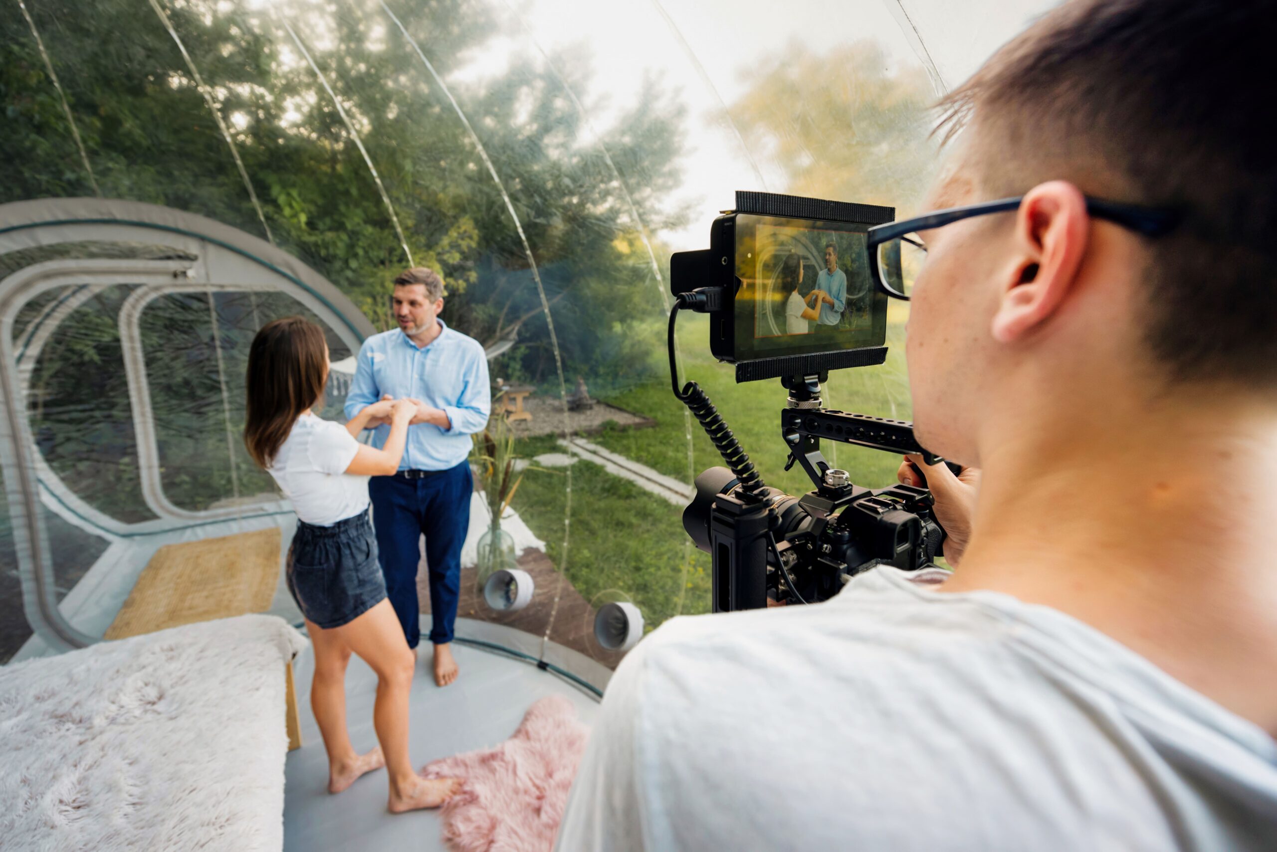 camera-man-filming-couple-inside-transparent-bubble-tent-glamping-professional-camera